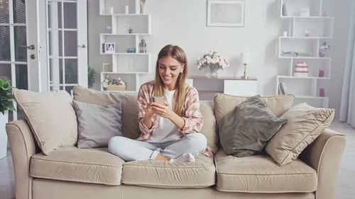 Smiling Woman Using Mobile Phone on Sofa Indoors