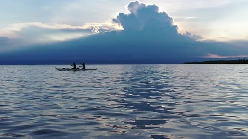 People Silhouetted Paddling Boat on Water at Sunset