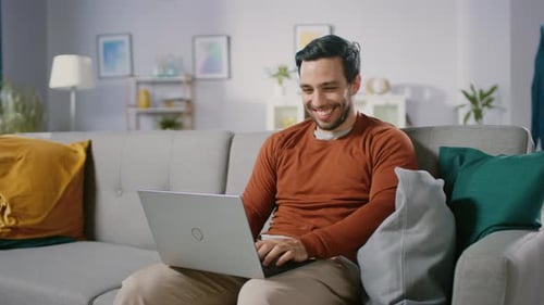Man Smiling, Using Laptop on Couch in Living Room