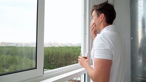 Man Drinks Cup of Coffee on Balcony Overlooking Forest