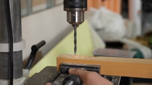 A Male Carpenter Drilling a Hole in a Wooden Bar with a Drill in a Workshop