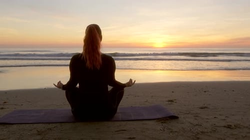 Woman meditating while holding lotus flower looking at the sea during sunrise