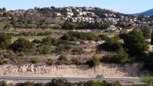 Drehdrohnenaufnahmen von drei Teamradfahrern, die auf einer ländlichen Asphaltstraße in einem Tal auf einer heißen Straße fahren