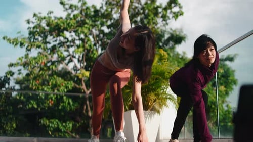 Women practicing yoga outdoors on balcony in sunshine