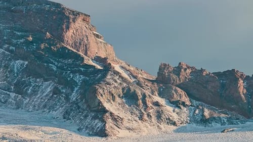Aerial drone view of rugged rocky mountain cliffs covered in snow, illuminated by soft winter sunlig