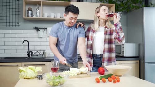 Couple Preparing Salad with Wine in Kitchen