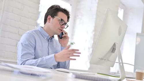 Serious Working Young Man Talking on Smartphone and Discussing Work