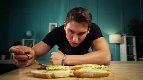 Man Spreads Avocado on Toast Indoors