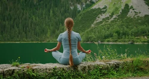 Woman with long braided hair meditating by a tranquil alpine lake in Austria