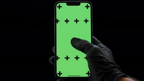 Un geste de balayage latéral sur l'écran d'un smartphone avec un écran vert, la main dans un gant en nitrile noir.