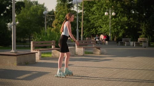 Woman Skating Slowly in Park with Benches and Sunlit Greenery in Background