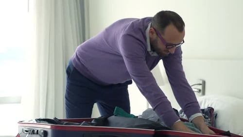 Man Packing Clothes into Suitcase in Hotel Room