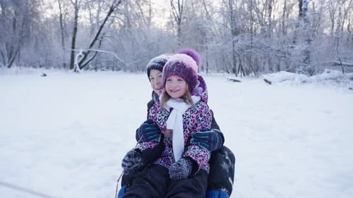 Glückliche Mutter reitet Kinder auf Schlitten in einem verschneiten Wald