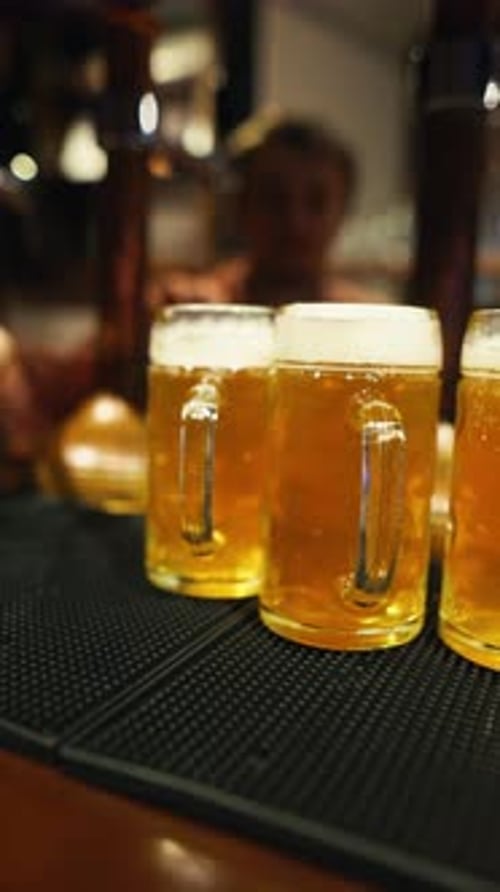 Three Frothy Beer Mugs are Placed on the Counter of a Bar with a Blurred Background