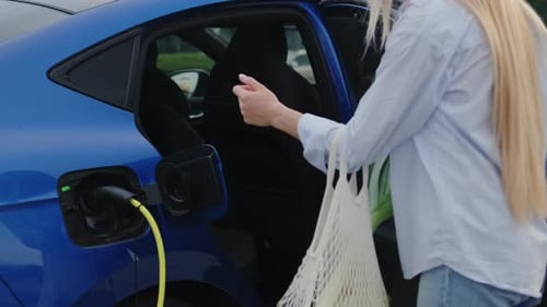 Mujer pone una bolsa de la compra en un salón de autos eléctricos en la estación