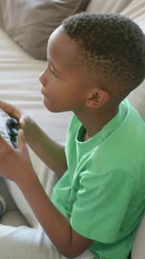 Vertikales Video: Spielendes Kind mit Controller im grünen Tee auf der Couch, Spiel starten und reagieren