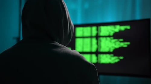Closeup View From Shoulder of Unrecognizable Male Hacker in Sweatshirt with Hood Typing on Keyboard
