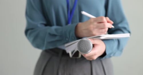 Journalist with microphone taking notes on light background, closeup