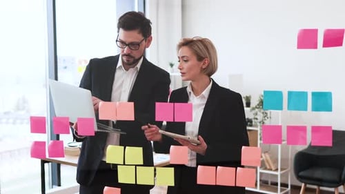 Professional Team Collaborating with Sticky Notes and Devices on Glass Board
