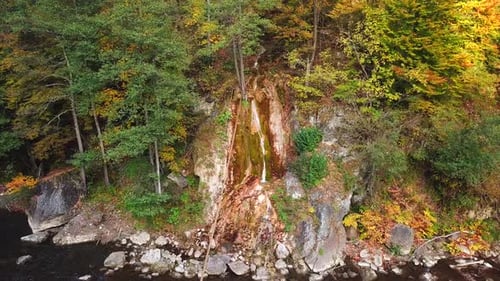 Luftaufnahme eines kleinen Wasserfalls, der eine felsige Klippe hinunterfließt, umgeben von Herbstbäumen