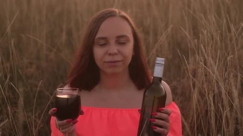 Young Woman in Bright Dress with Short Hair Drinking Red Wine From Glass Holding Bottle of Wine