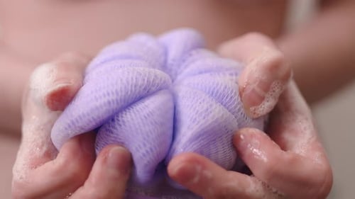 Woman Squeezing Purple Bath Sponge with Soap