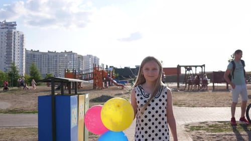 Beautiful Little Girl with Balloons Walks Through the Children's Amusement Park in Summer