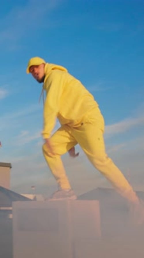 Tanzender Mann in gelbem, hellem Outfit, Breakdance auf dem Dach, Hip-Hop-Bboy-Tänzer, der Stunts aufführt