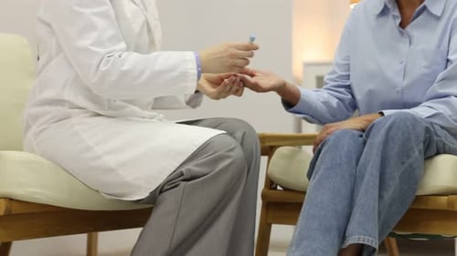 Diabetes. Doctor checking patient's blood sugar level with lancet pen and glucometer on armchair