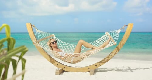 Idyllic Scene. Beautiful Woman Sunbathing Lying in Hammock on a Beach. Azure Beach with White Sands