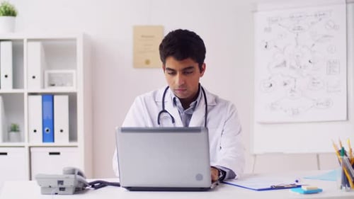 Indian doctor at hospital using laptop and phone for healthcare communication