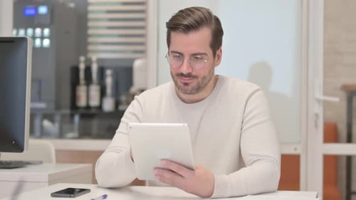 Young Man Celebrates Success Using Tablet in Office