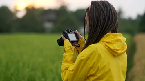 Photographer with Dreadlocks and Yellow Raincoat Taking Pictures in a Field at Sunset