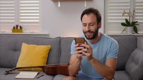 Man Smiling at Phone on Couch at Home