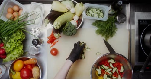 Top-view of woman hands cutting cucumber and adding it into salad bowl