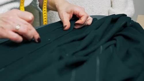Nahaufnahme in einer Nähwerkstatt Die Schneiderin misst auf einem schwarzen Stoff, wo man sie feststecken muss