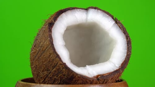 Cracked fresh coconut spinning. Coconut rotates on a green background in a wooden bowl. Making
