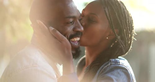Candid African couple together outside at park. Woman kissing man in cheek outside