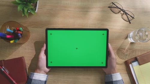 Top down view of man's hands holding a mock up green screen tablet on a desk
