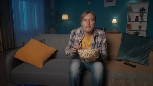 Horror Film Shocked Man Watching a Scary Movie on TV at Home and Eating Popcorn The Man Shudders in