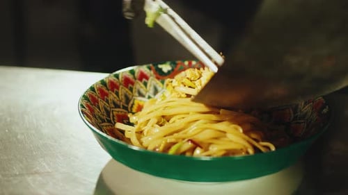 Chef Plating Pad Thai Noodles Into Colorful Bowl in Restaurant