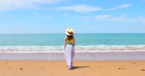 Attraktive Frau mit Strohhut und winkendem Rock steht am Sandstrand