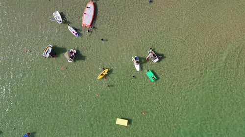 Menschen auf verschiedenen bunten schwimmenden Matten und kleinen Booten am Strand.