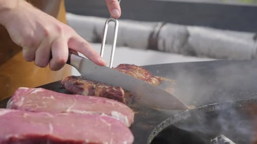 Chef slicing juicy beef steak on outdoor grill. Close-up of a chef cooking and slicing a delicious