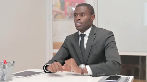 Wartender afrikanischer Geschäftsmann überprüft die Zeit auf der Armbanduhr, während er im Büro sitzt