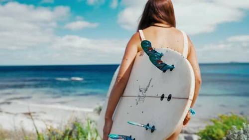 Surfer walks towards the ocean with a surfboard on a sunny day in a coastal area