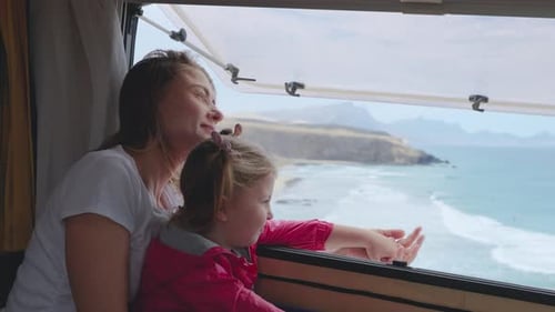Cheerful Mother and Daughter Look Out of the Camper Window at Ocean or Sea Waves Family Holidays