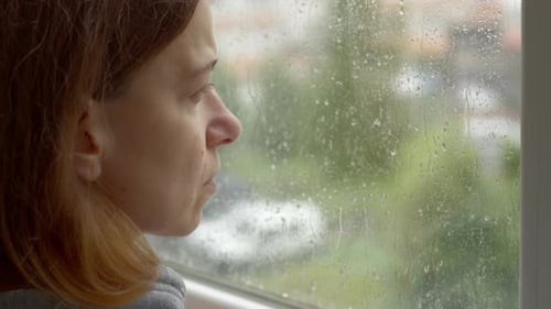Das Gesicht einer nachdenklichen und traurigen Frau, die mit Regentropfen aus dem Fenster schaut. psychische Gesundheit.