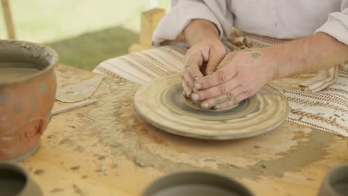 Les mains d'un potier centrent un morceau d'argile humide sur un tour de poterie traditionnel.
