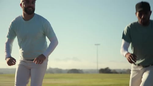 Facing each other baseball partners jogging and side shuffling on field with batting cage nets